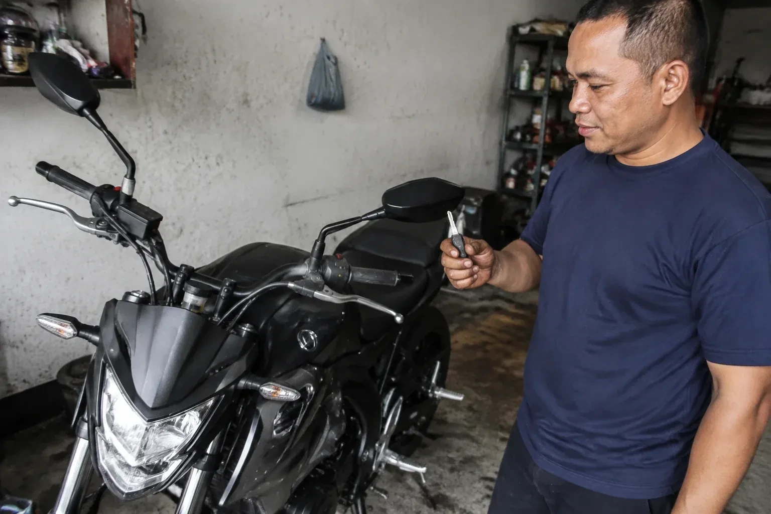 Person holding a key beside a black motorcycle in a garage. — Motorcycle & Scooter Keys, Pickering