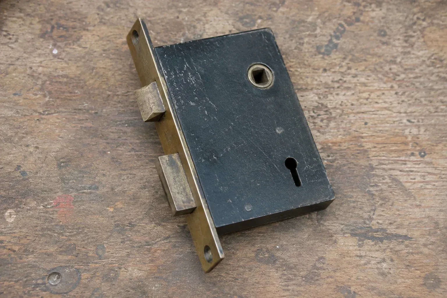Closed mortise lock case with spindle opening, keyhole, latch and deadbolt on a wooden workbench. — Vintage Mortise Lock Service, Pickering