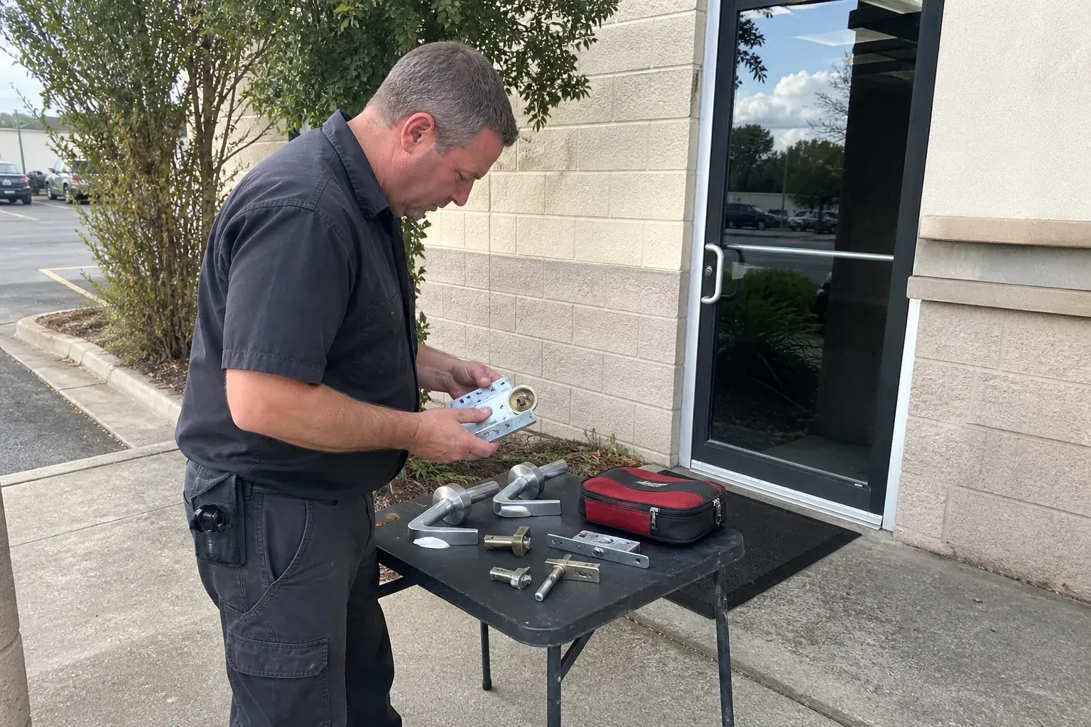 Technician examining detached commercial lock hardware on a table outside a shop entrance. — Business Lockout Service, Pickering