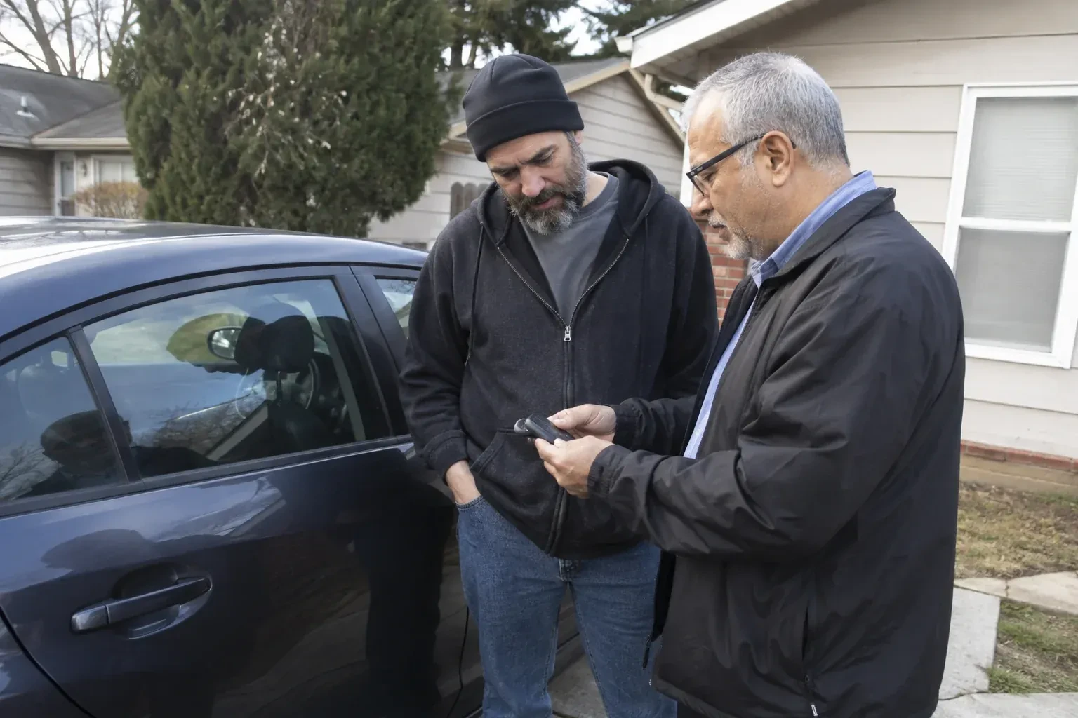 Two adults discussing a key fob beside a parked car. — Car Lockout Service, Pickering